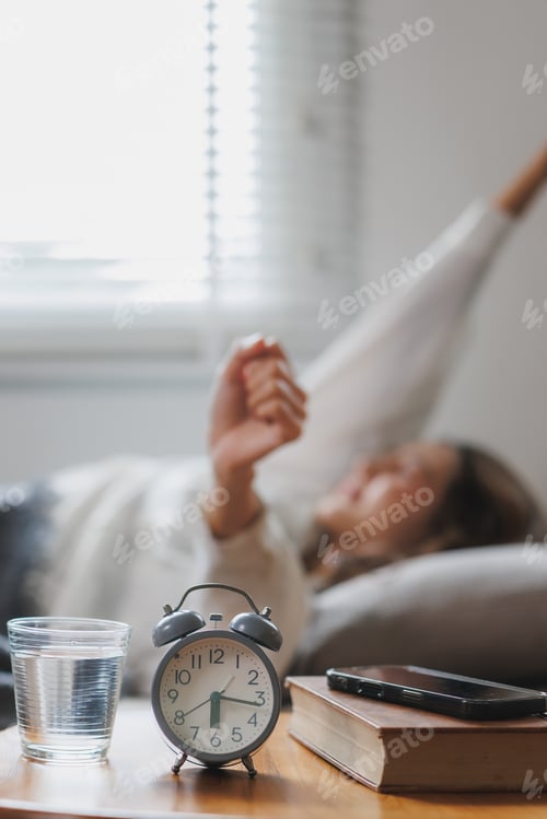 Preview: Woman waking up and stretching in bed after alarm clock rings