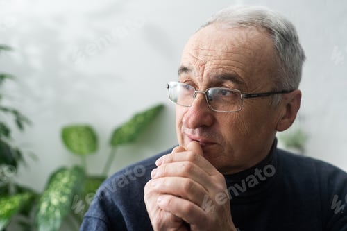 Preview: Worried religious senior man praying to god with his hands raised and touching as he looks