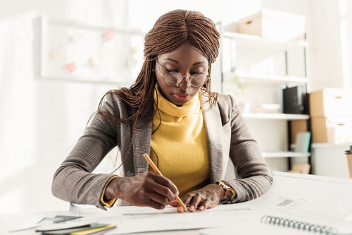 Preview: concentrated african american female architect in glasses holding pencil and working on project at
