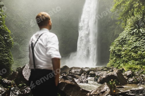 Preview: Traveller man looking on huge waterfall Nung-Nung in Bali Jungle. Asia travel concept. Amazing view.