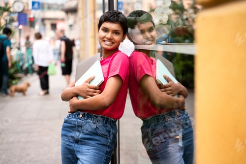 Preview: Smiling asian student holding book, laptop looking at camera standing outdoors