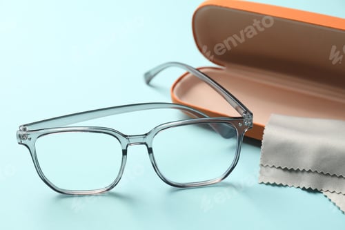 Preview: Case, stylish glasses and cleaning cloth on light blue background, closeup