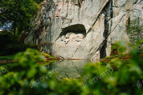 Preview: The Lion Monument in Lucerne, Switzerland, reflecting in a pond surrounded by greenery