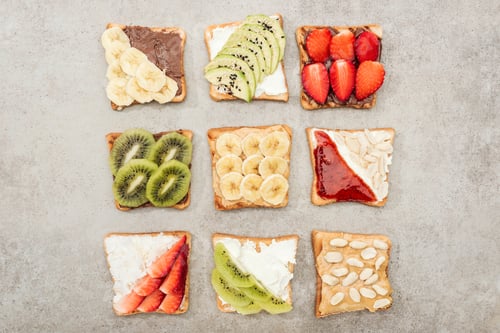 Preview: Top view of toasts with cut fruits, berries and peanuts on textured surface