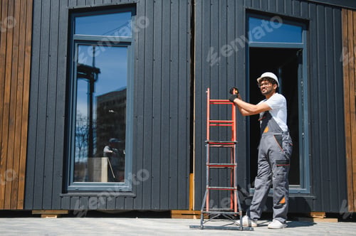 Preview: Construction worker holding a ladder next to modular house