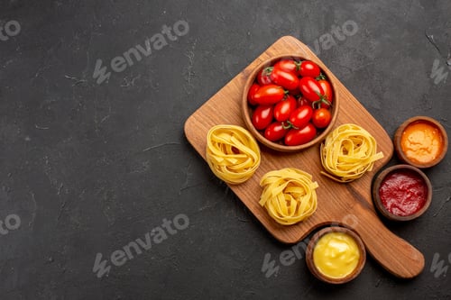 Preview: top view pasta and sauces tomatoes and pasta on the cutting board and different sauces on the dark