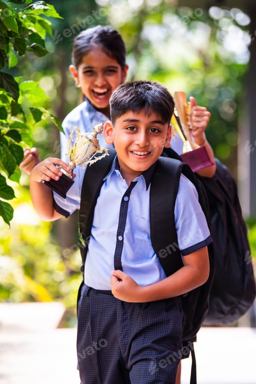 Preview: Indian School Kids in Uniform Flaunting Trophy Proudly While Standing Outside and Looking at Camera