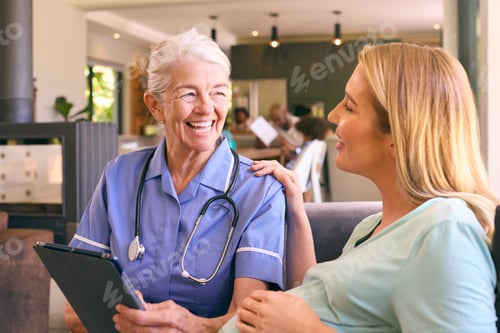 Preview: Senior Midwife With Digital Tablet Visiting Pregnant Woman At Home With Family In Background