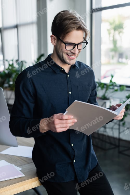 Preview: Young programmer looking at paper folder near computer in office