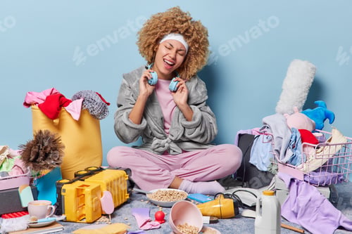 Preview: Positive housewife sings song feels glad sits in lotus pose on floor with different household items