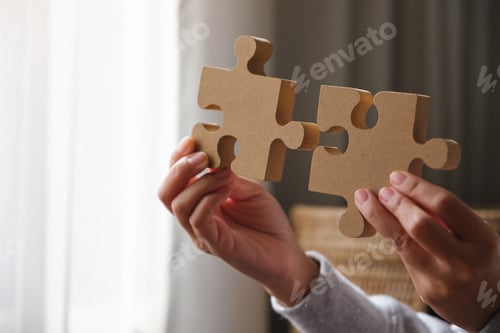 Preview: Closeup image of hands holding and putting a piece of wooden jigsaw puzzle together