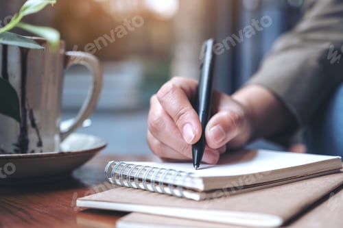 Preview: Closeup image of a woman's hand writing on blank notebook with coffee cup on wooden table