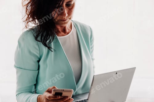 Preview: Focused Woman Working with Laptop and Phone Indoors