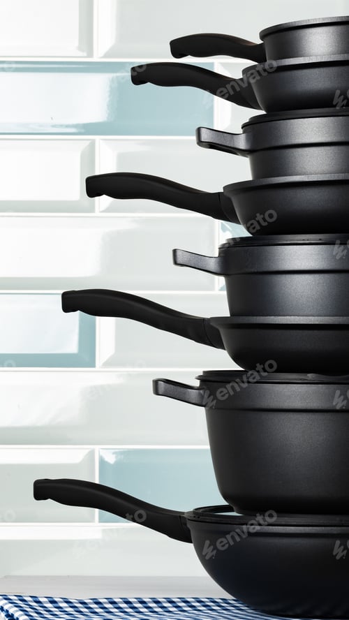 Preview: Stack of black cooking pots on a blue and white checkered cloth in a kitchen setting