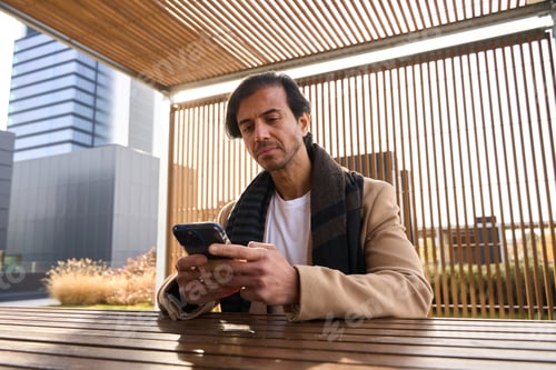 Preview: Man typing message on phone in urban outdoor cafe setting