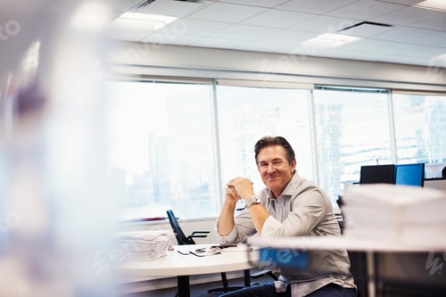 Preview: A man sitting at a table in an office, looking into shot and smiling.