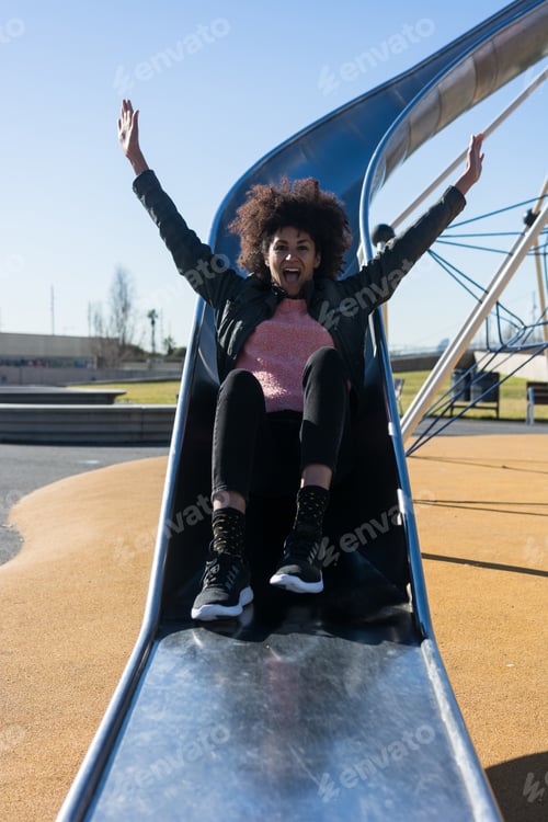 Preview: Woman with afro hair jumping down a slide.