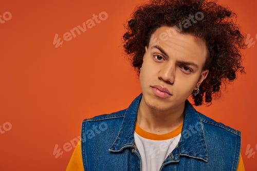 Preview: attractive young african american man in casual urban attire posing emotionally on orange background