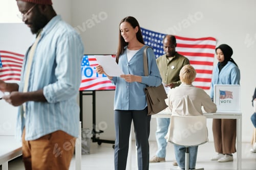 Preview: Happy young woman looking through ballot paper at polling place
