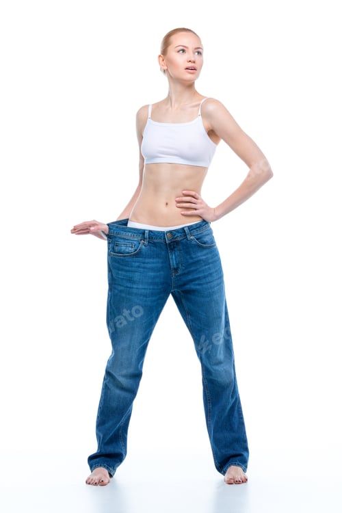 Preview: Young slim woman in oversized jeans standing with hand on waist and looking away isolated on white
