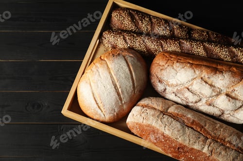 Preview: Basket with different types of fresh bread on black wooden table, top view. Space for text