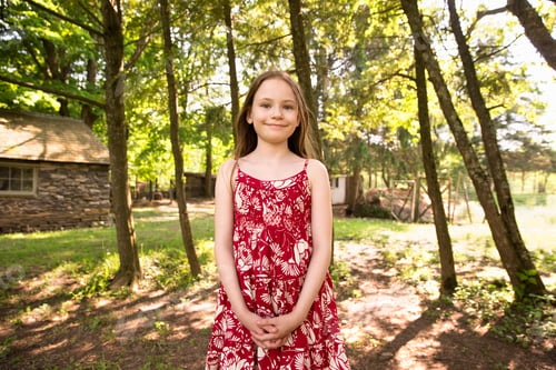 Preview: A girl in a summer dress standing in a grove of trees.