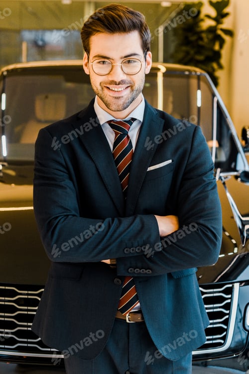 Preview: laughing businessman in eyeglasses posing with crossed arms near black automobile