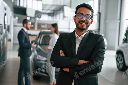 Preview: Man standing in front of his coworkers. Three people are working together in the car showroom