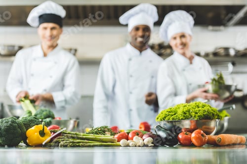 Preview: smiling multicultural chefs at restaurant kitchen with vegetables on foreground
