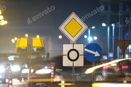 Preview: Roundabout road signs with blurred cars on city street traffic at night.