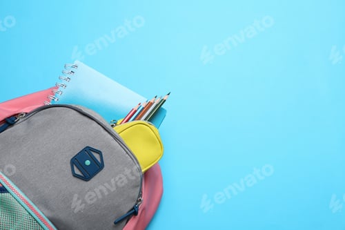 Preview: Stylish backpack with different school supplies on light blue background, top view. Space for text