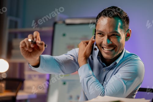 Preview: Asian man talking on the phone in the office of a startup company, company employees working overtim