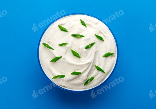 Preview: Bowl of sour cream on blue background, top view