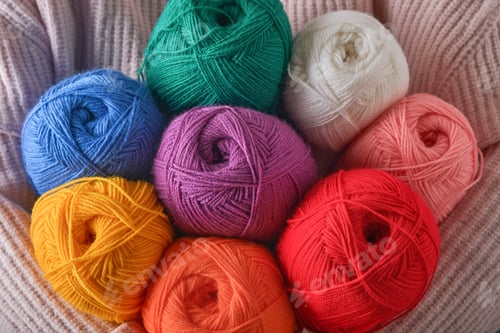 Preview: Female holding colorful or multicolored wool yarns on blue background. Many multi-colored balls of t