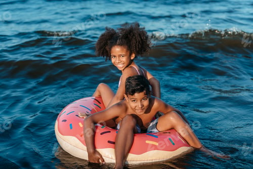 Preview: adorable african american siblings sitting on swimming tube and smiling at camera