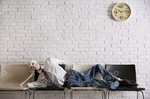 Preview: Human skeleton in office wear lying on chairs near brick wall indoors