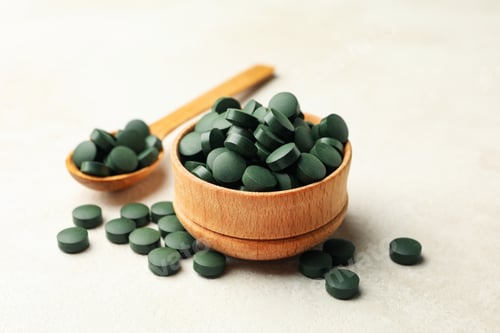 Preview: Wooden bowl and spoon with spirulina pills on white textured background