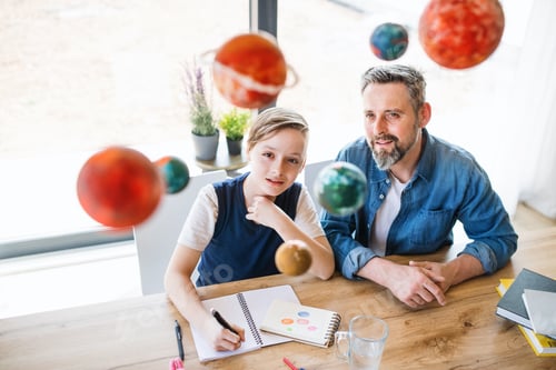 Preview: Mature father with small son sitting at table indoors, working on school project