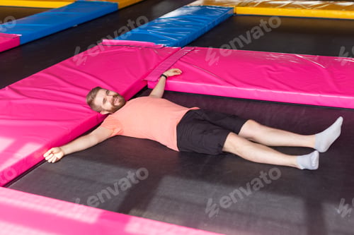Preview: Fitness, fun, leisure and sport activity concept - Man lying on a trampoline indoors, top view