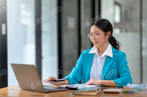 Preview: Focused businesswoman working on a laptop at a wooden desk.