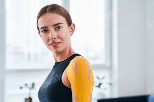 Preview: Happy cheerful female with yellow tapes on her shoulder standing in medical office