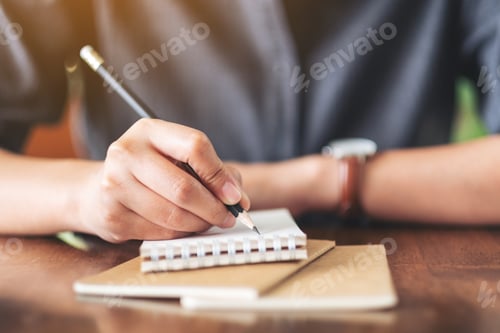 Preview: Closeup image of a woman writing on blank notebook with coffee cup on table in cafe