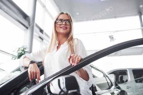 Preview: In eyewear. Young manager in the auto shop stands against perfectly polished black car