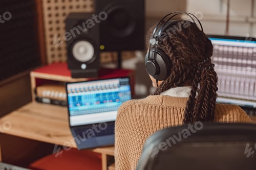 Preview: Musician with headphones sitting at desk with laptop while recording new song in the music studio