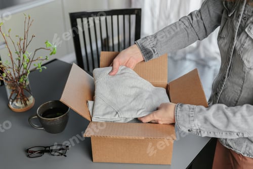 Preview: Woman packing donate cardboard box with clothes for charity