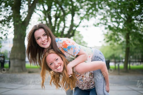 Preview: Portrait of two young female best friends giving piggy back in park