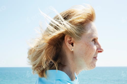 Preview: Profile of a blond mature woman standing by the ocean.