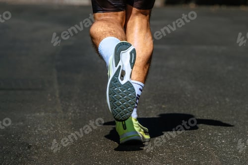 Preview: close-up sole running shoe and legs male runner, background dark road, marathon race