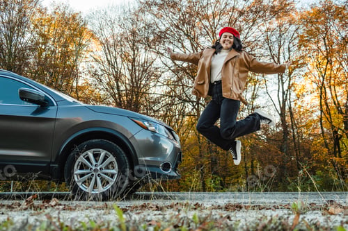 Preview: happy smiling woman jumping near the car on the background of autumn trees