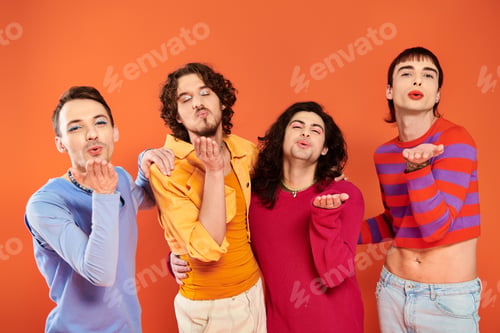 Preview: four stylish cheerful gay men in vibrant clothes posing together on orange backdrop, pride month